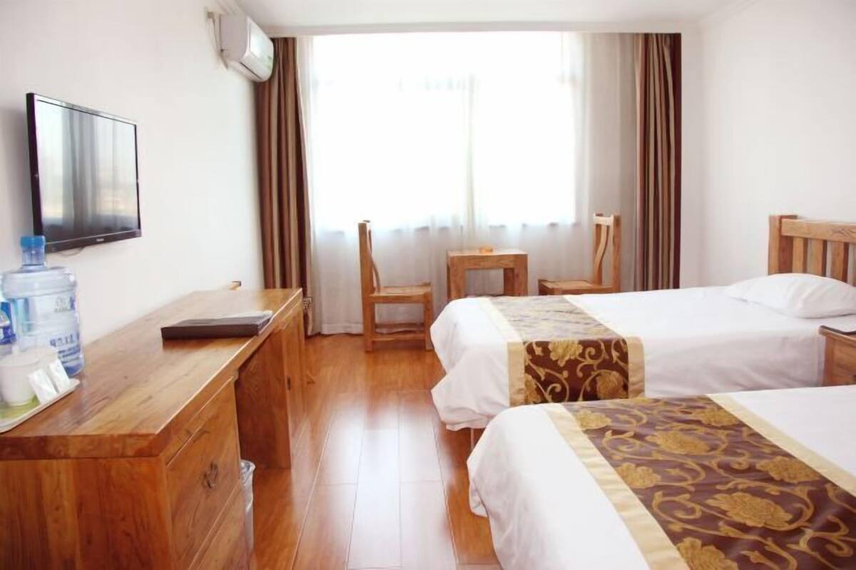 A hotel room with two beds, a wooden desk, a television, and a window with curtains.