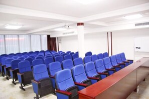 Un salón de conferencias con filas de sillas azules, una larga mesa de madera y una pizarra.