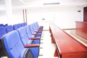 Une salle de conférence avec des rangées de chaises bleues, une table en bois et un plafond blanc.
