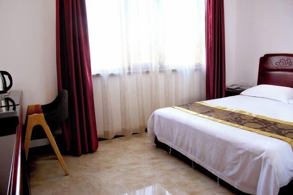 Een hotelkamer met een bed, een bureau met stoel, en een raam met gordijnen.