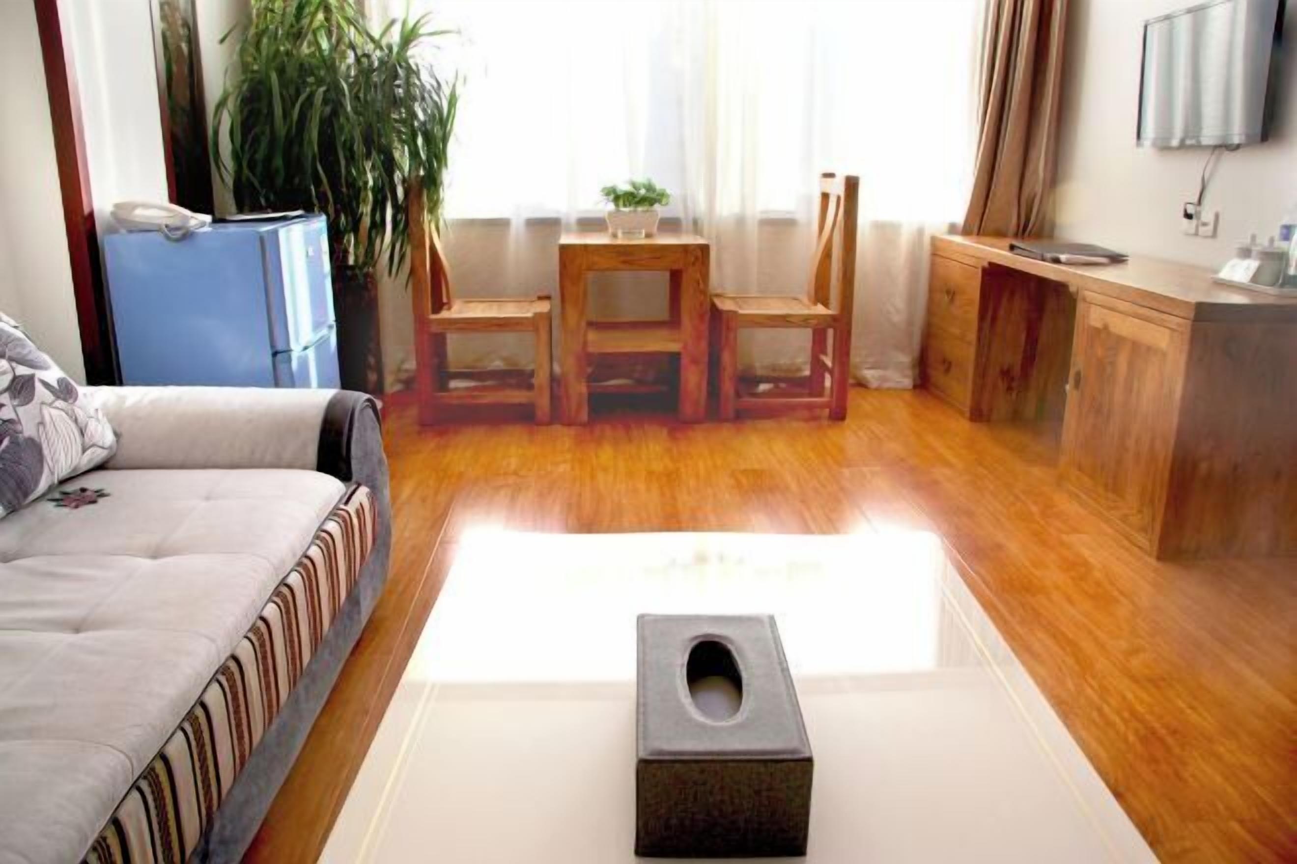 A room with a sofa, a small table with chairs, a wooden cabinet, and a trash bin.