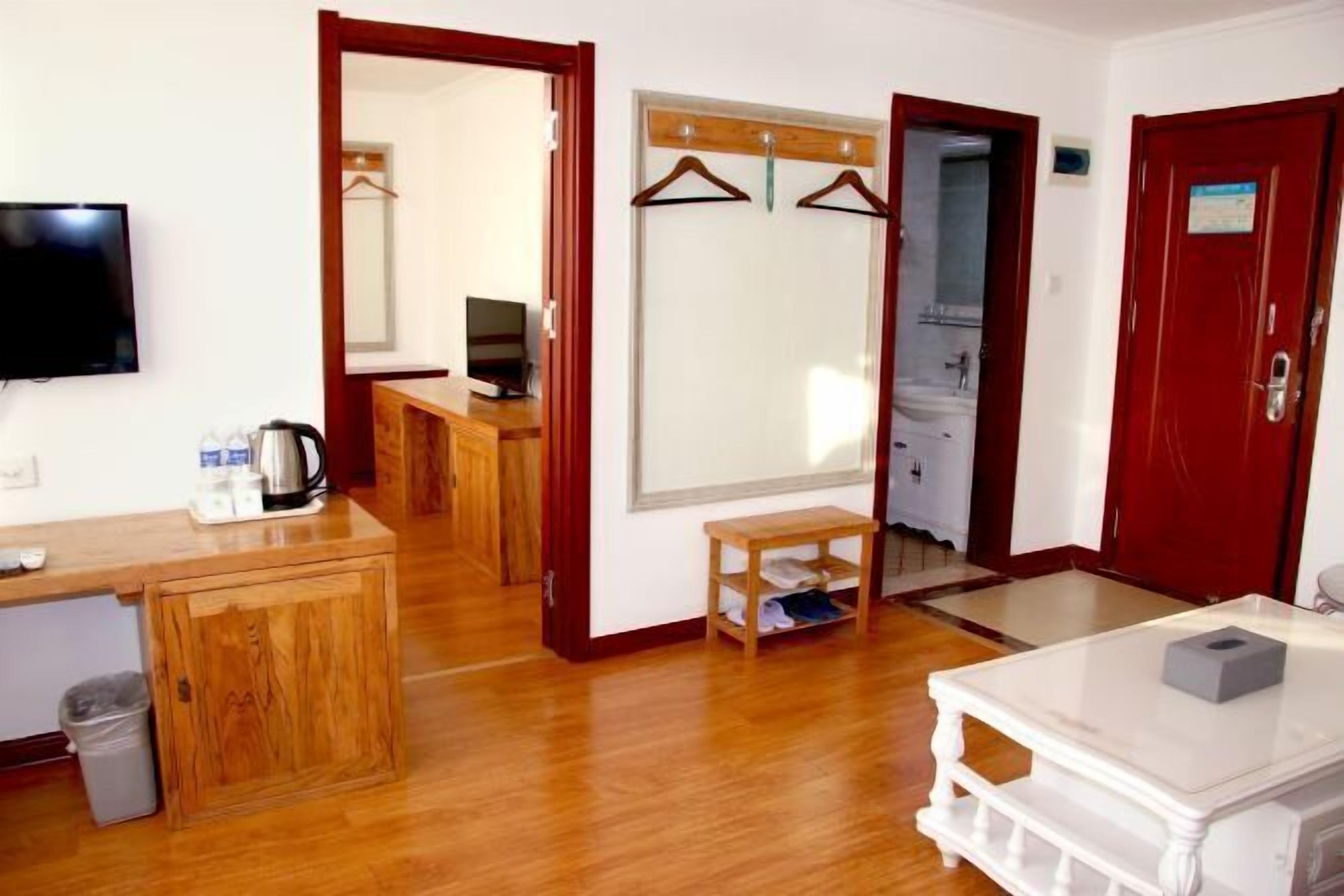 A hotel room with a wooden desk, a television, a mirror, a wardrobe, and a small table with a tissue box.