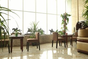 Um saguão com uma janela grande, algumas cadeiras, um sofá e plantas em vasos.