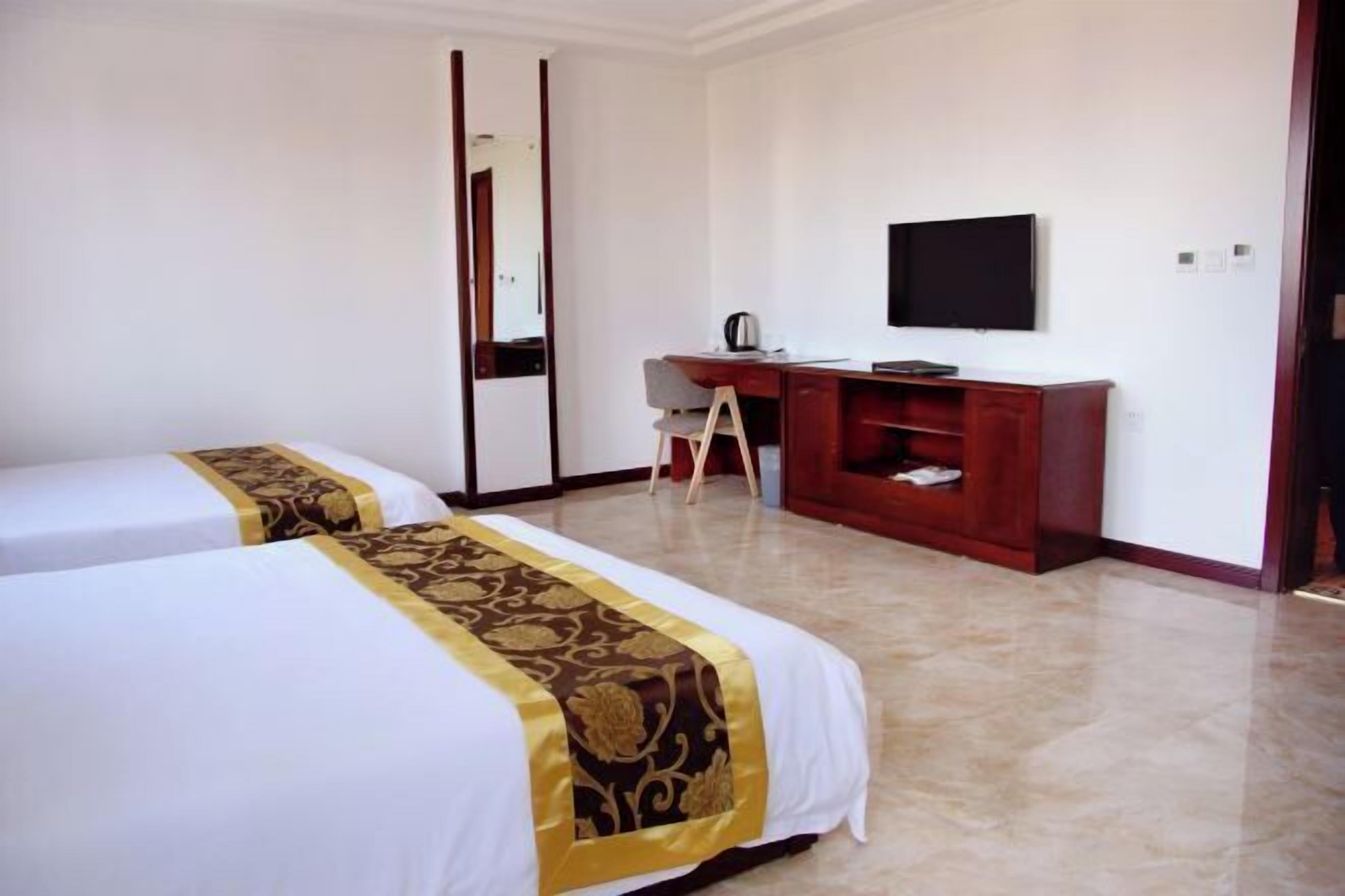 A hotel room with two beds, a desk, a chair, a TV, and a wardrobe.