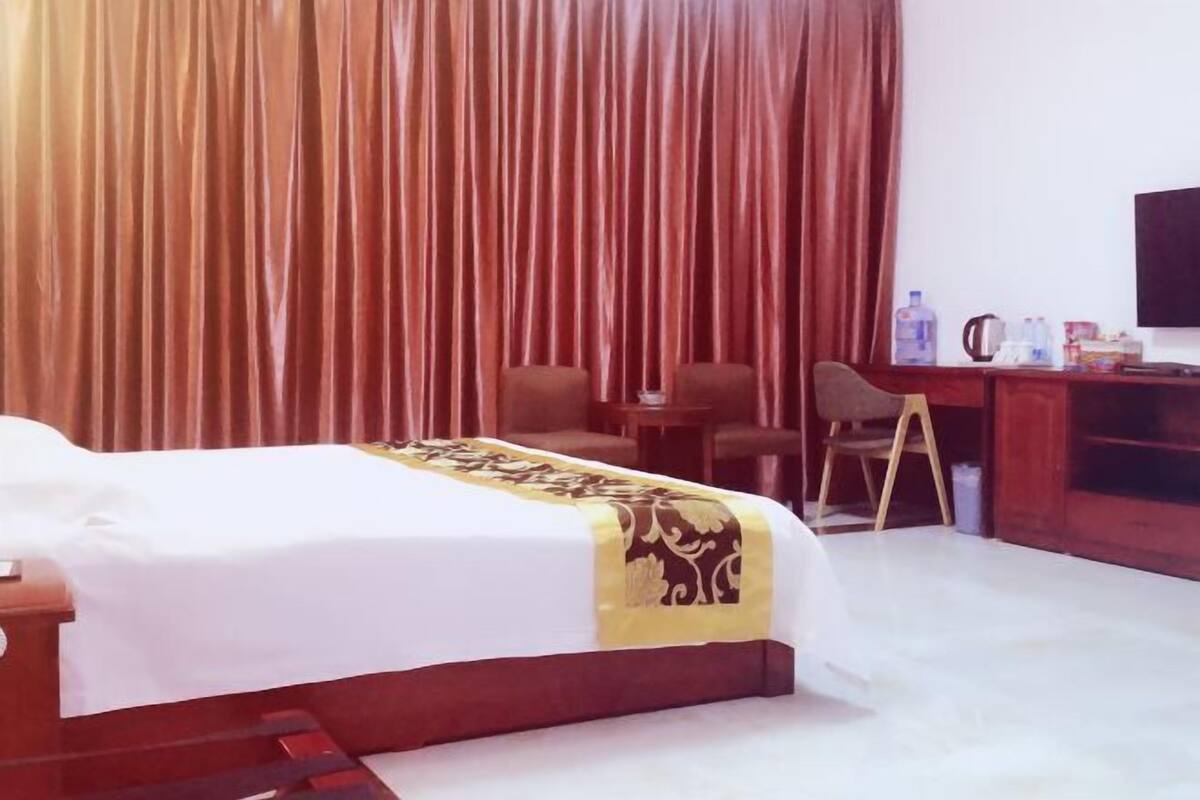 A hotel room with a bed, a desk, a chair, a television, and a curtain.