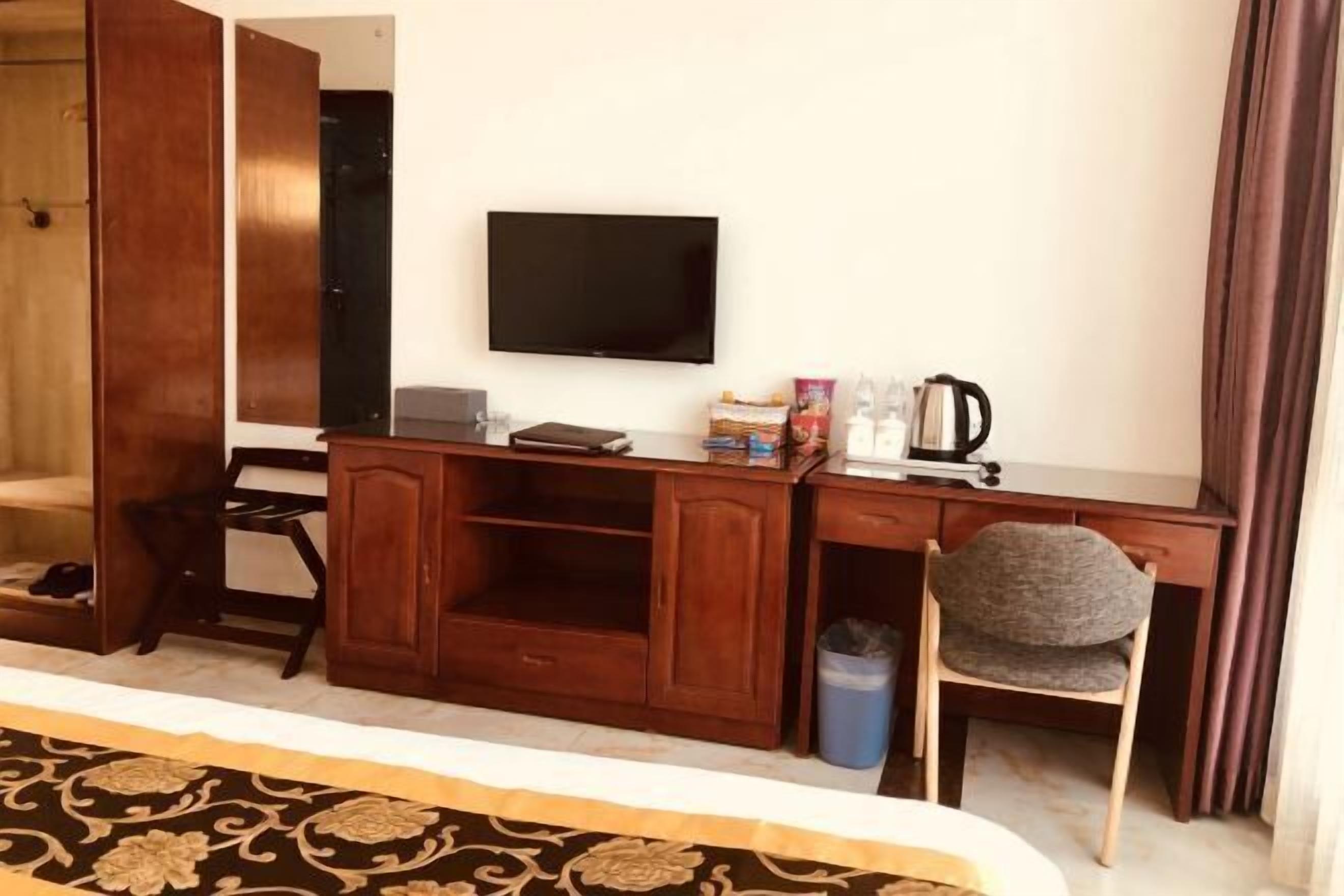 A hotel room with a wooden desk, a television, a chair, and a patterned carpet.