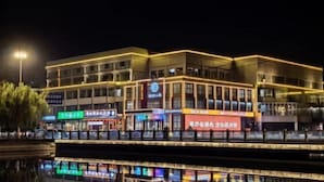 Ein mehrstöckiges Gebäude mit beleuchteter Beschilderung, einem sich spiegelnden Wasserspiegel davor und einer Straßenlaterne in der Nähe.