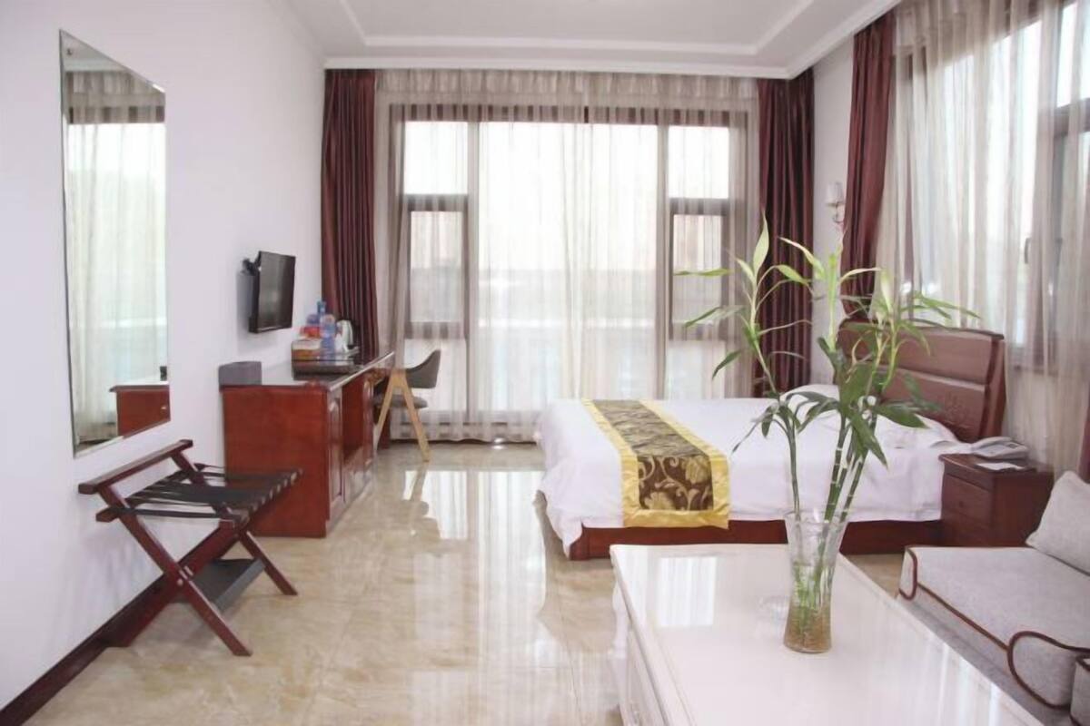 A hotel room with a bed, a desk, a chair, a mirror, a television, and a plant.
