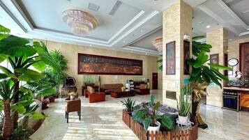 A spacious lobby with a high ceiling, large windows, and a central seating area surrounded by potted plants.