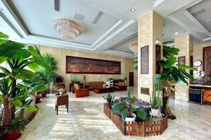A spacious lobby with a high ceiling, large windows, and a central seating area surrounded by potted plants.