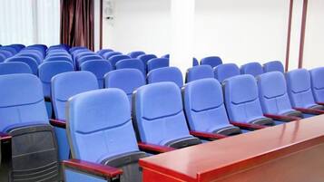 Uma sala de conferências com fileiras de cadeiras azuis e uma mesa de madeira.