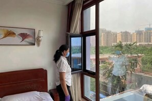 Quarto de hotel com uma janela grande, uma cama, luminária na parede e um quadro.