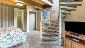 Ein Schlafzimmer mit einem Bett, einem Fernseher, einer Treppe und einer Tür zu einem anderen Raum.