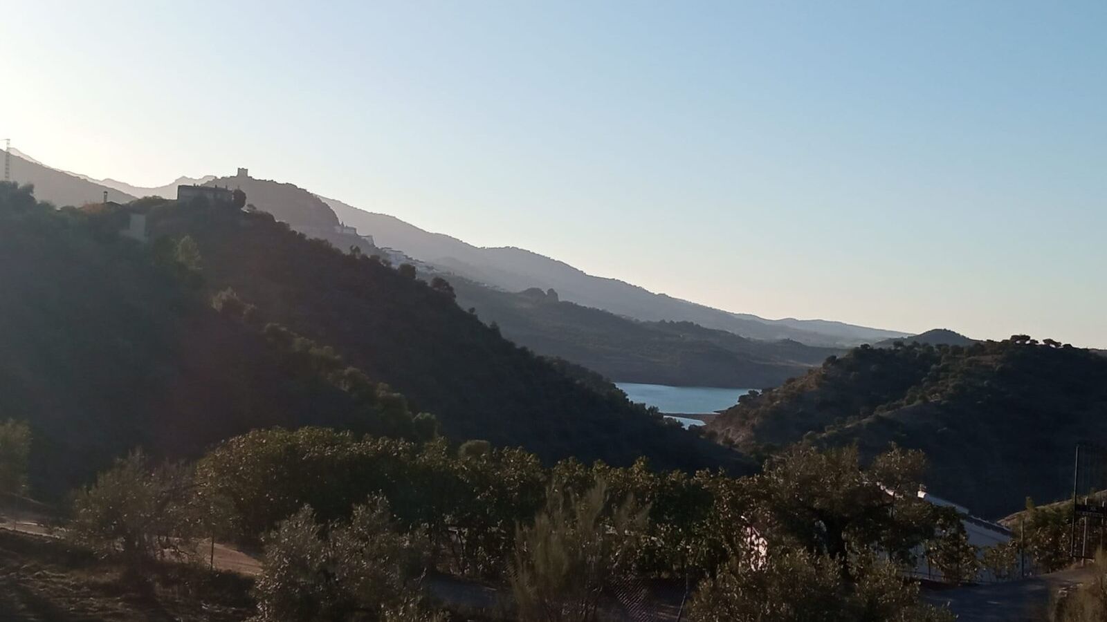 A mountainous landscape with a lake and a building on a hill.