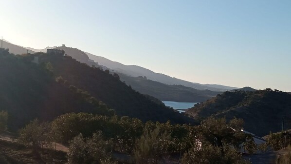 Paisaje montañoso con un lago y un edificio en una colina.