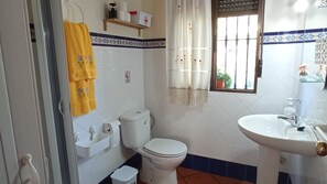 Casa de banho com sanita, lavatório e janela com vista para vegetação lá fora.