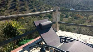 A balcony with a lounge chair, a stone wall, and a view of a hilly landscape. - Villa Aurora El Gastor by Ruralidays (Cádiz)
