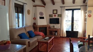 A living room with a sofa, coffee table, fireplace, and a TV mounted on the wall. - Villa Aurora El Gastor by Ruralidays (Cádiz)