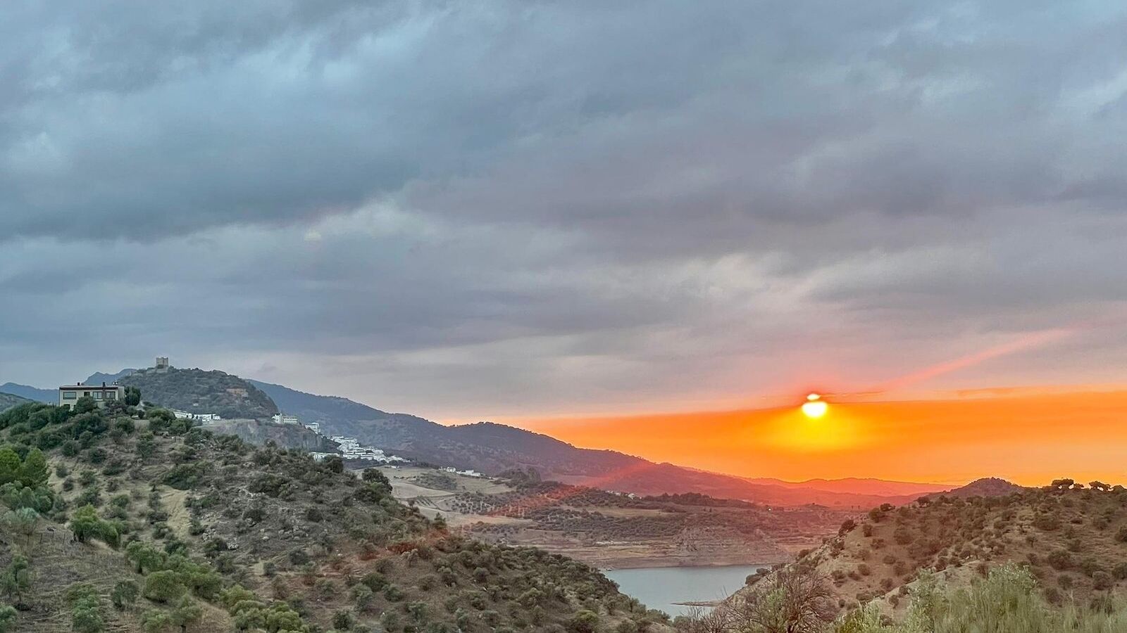Un atardecer sobre un paisaje montañoso con un edificio a la izquierda.