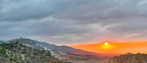 Un atardecer sobre un paisaje montañoso con un edificio a la izquierda.