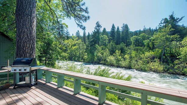A wooden deck with a grill and a view of a river surrounded by trees.