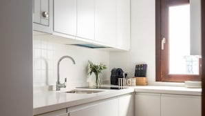 Cozinha moderna com armários brancos, pia de aço inoxidável e janela com vista.