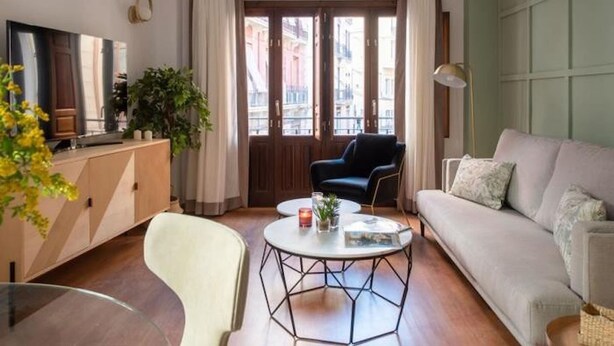 Uma sala de estar moderna com um sofá, uma poltrona, uma mesa de centro, uma televisão e vista da cidade através de grandes janelas.