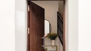 Uma porta de madeira dá acesso a um corredor com uma prateleira de metal que suporta um vaso com planta.