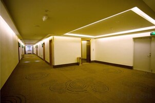 Un pasillo de hotel con pisos alfombrados, puertas e iluminación en el techo.
