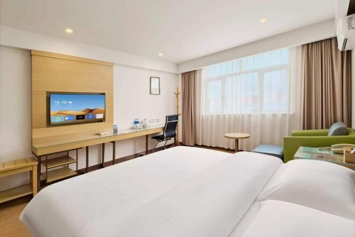 Habitación de hotel con cama, escritorio con televisor, silla, mesita y ventana con cortinas.