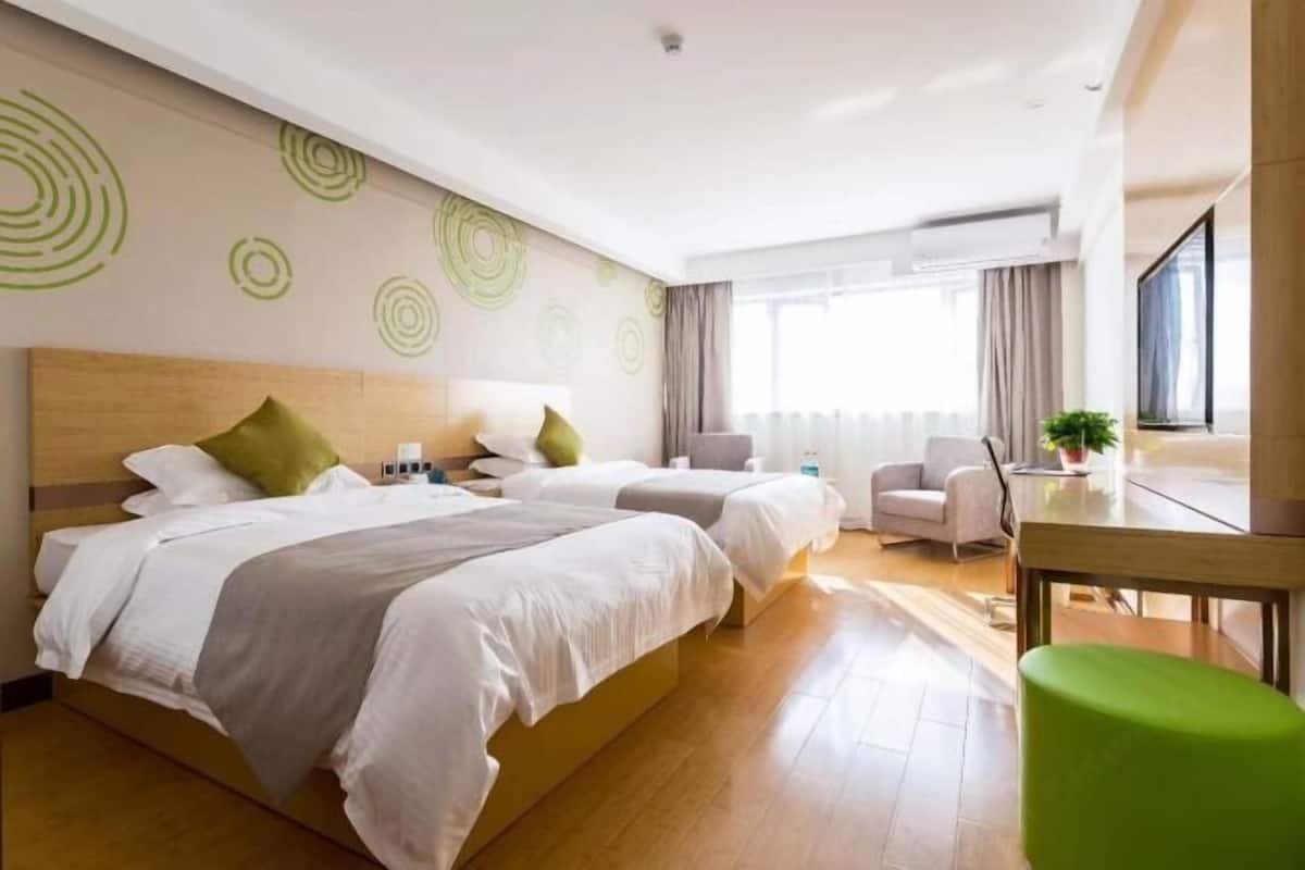 Habitación de hotel con dos camas, un escritorio, una silla y un ventanal con cortinas.