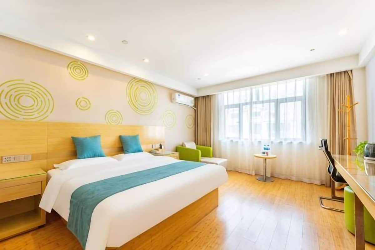 Habitación de hotel con una cama grande, una mesita, una silla, un escritorio y un ventanal con cortinas.