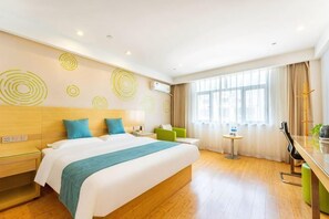 A hotel room with a large bed, a small table, a chair, a desk, and a window with curtains.