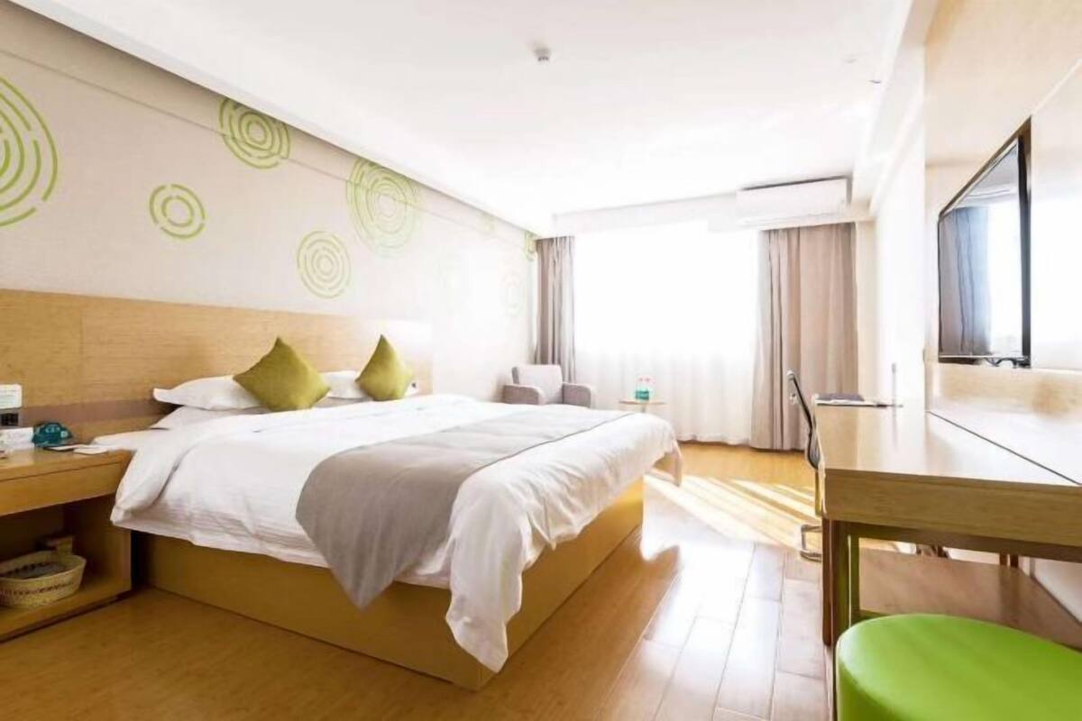 Habitación de hotel con cama, escritorio, silla, televisor y ventana con cortinas.