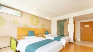 Ett hotellrum med två sängar, en sänggavel i trä, en grön stol och en dörr i trä.