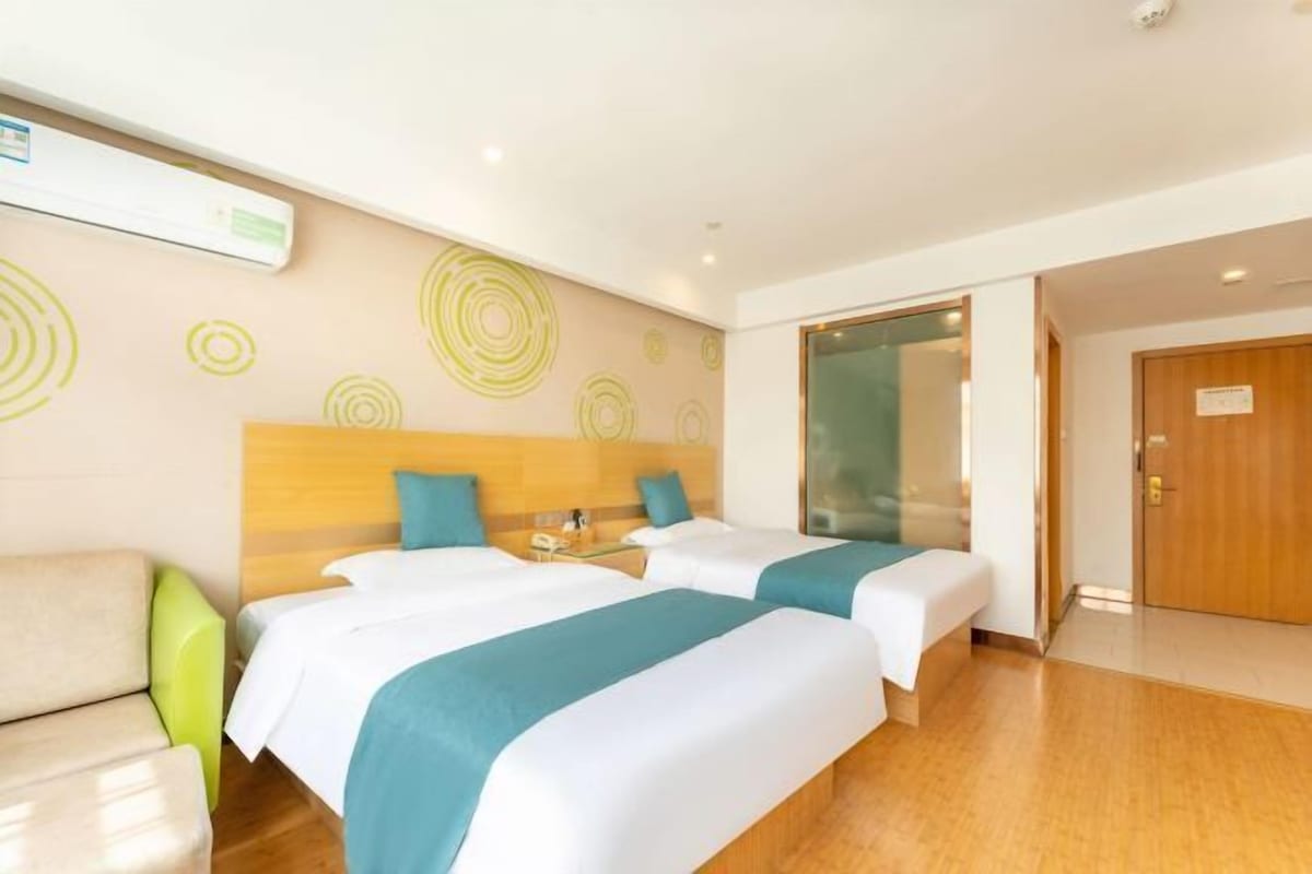A hotel room with two beds, a wooden headboard, a green chair, and a wooden door.