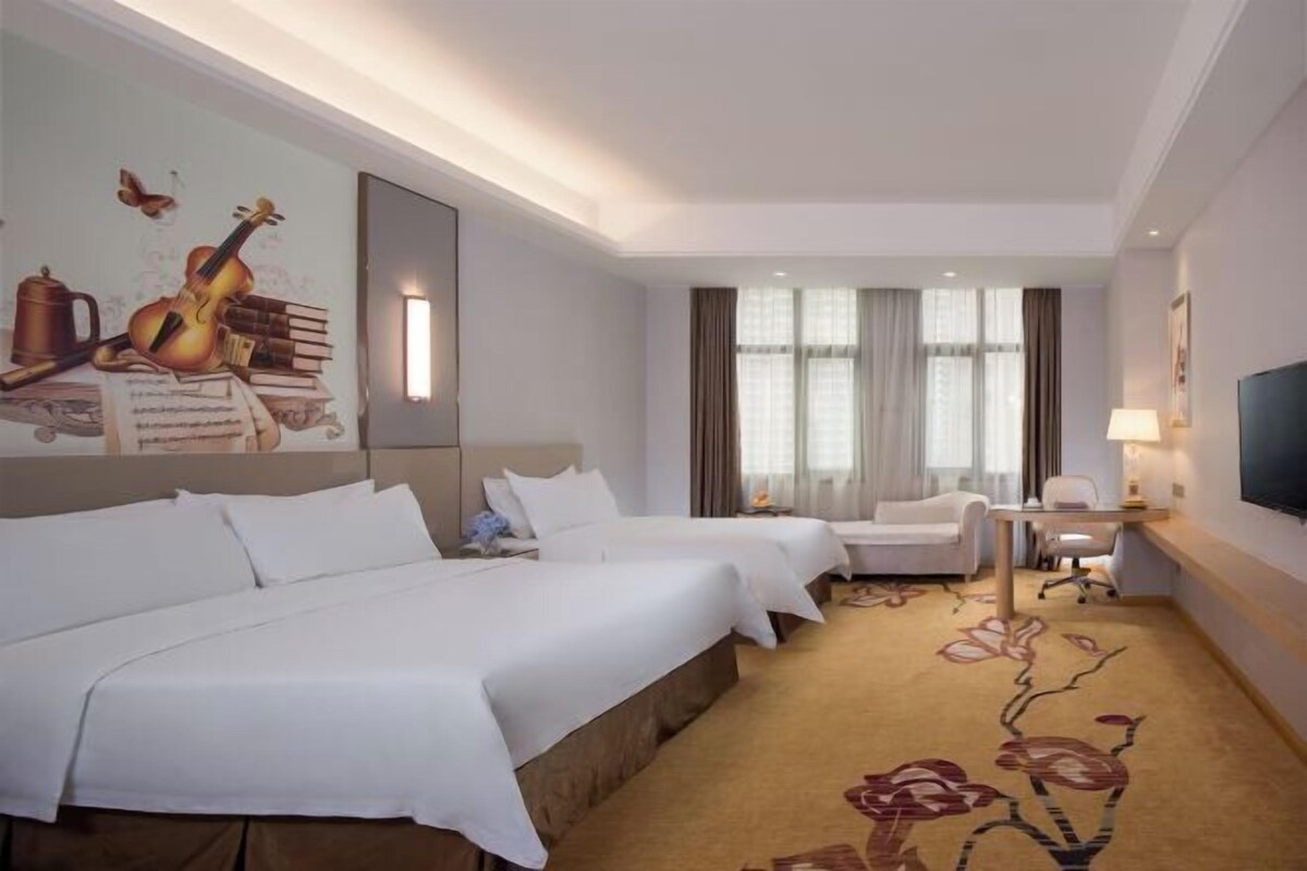 Habitación de hotel con dos camas, un escritorio, una silla, un televisor y una alfombra estampada con motivos florales.