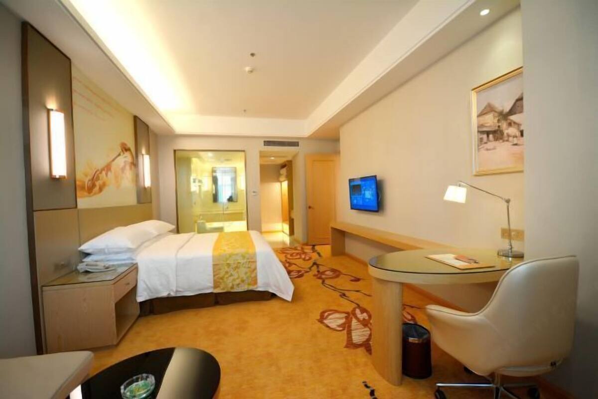 A hotel room with a bed, bedside table, desk, chair, and a TV on the wall.