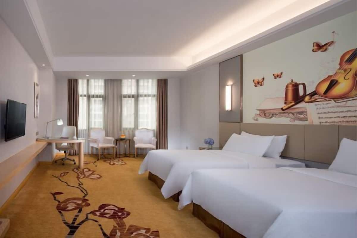 A hotel room with two beds, a desk with a chair, a TV, and a mural on the wall.