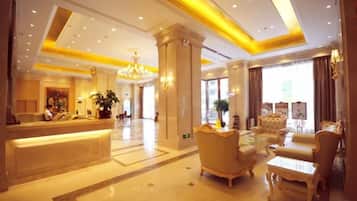 A hotel lobby with a reception desk, seating area, and a chandelier.