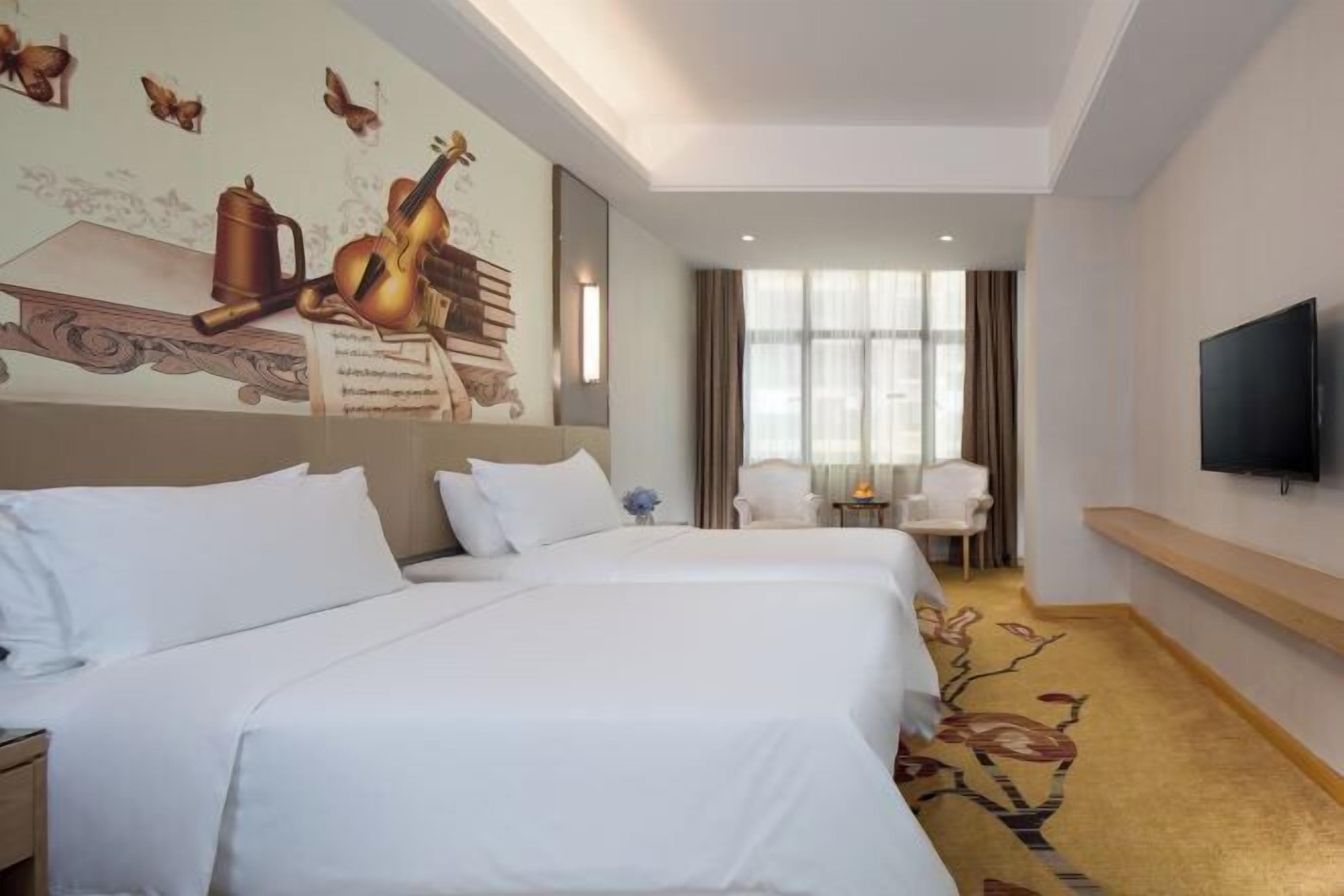 A hotel room with two beds, a television, a desk, and a window with curtains.