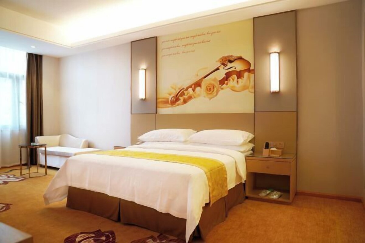 Una habitación de hotel con una cama grande, mesitas de noche, una silla y una lámpara fijada a la pared.