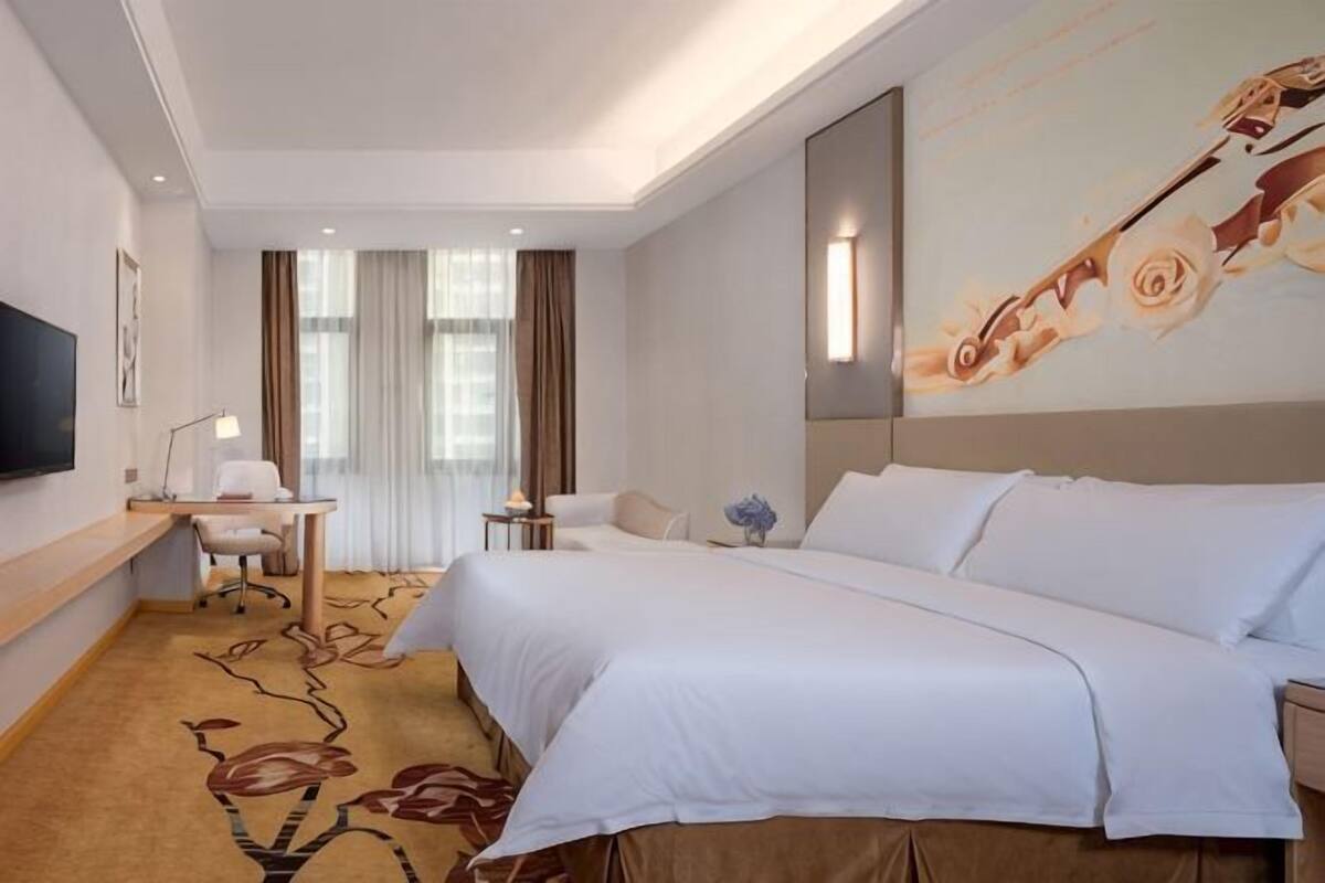 A hotel room with a large bed, a desk, a chair, a TV, and a painting on the wall.
