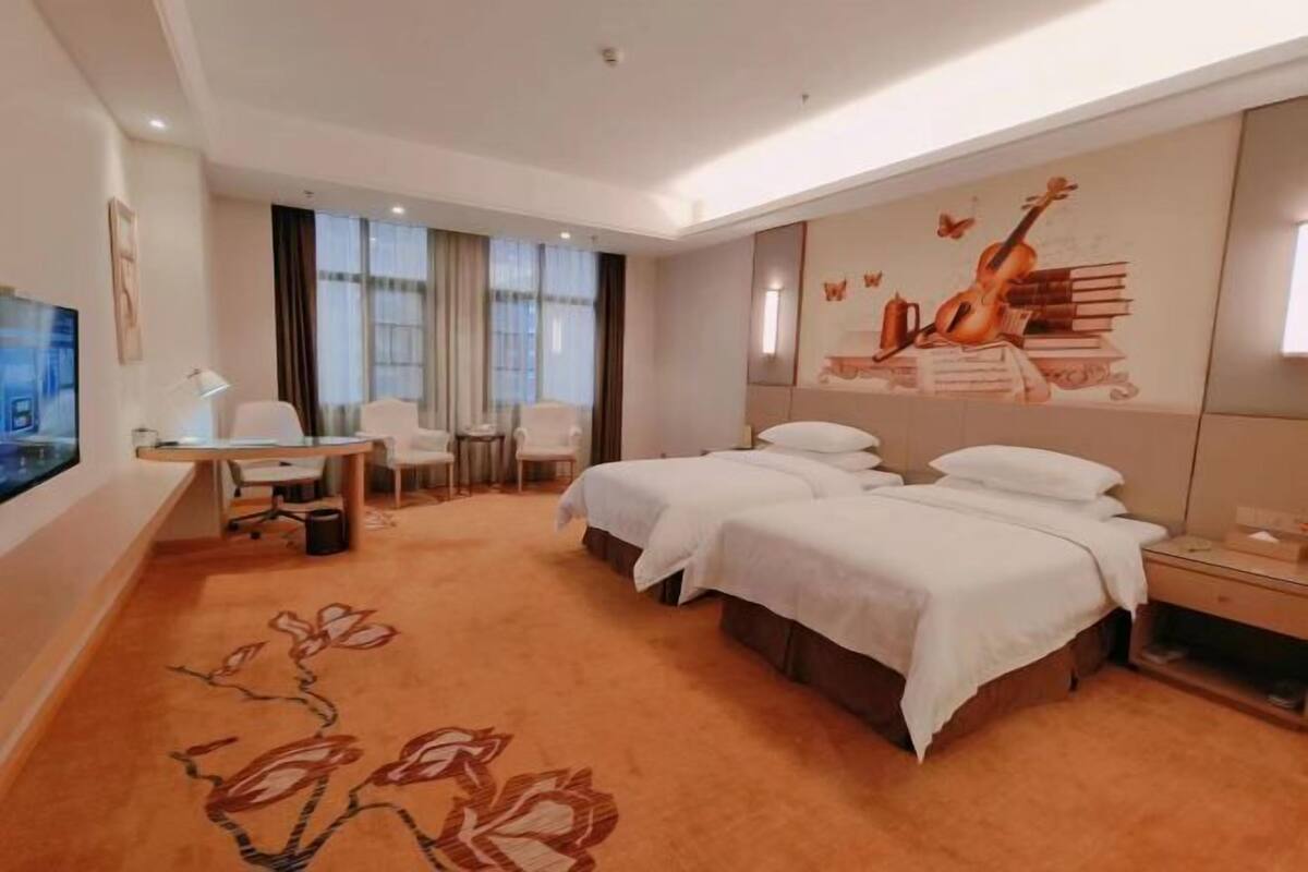 A hotel room with a bed, a desk, a chair, a TV, and a mural on the wall.