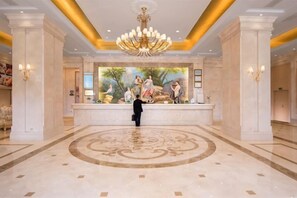 A grand lobby with a central reception desk, a large mural, and a chandelier. - Vienna International Hotel (Wugang Shaoyang) (Wugang)