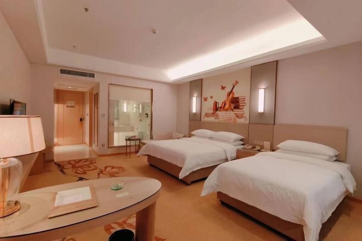 A hotel room with two beds, a desk, a lamp, a mirror, and a wall with a guitar and musical notes.