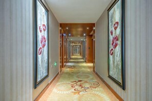 Corredor de hotel com piso em carpete, obras de arte nas paredes e teto de madeira.