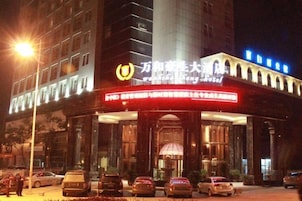 Un hotel con una entrada destacada, varios coches aparcados delante y un cartel iluminado grande sobre la entrada.