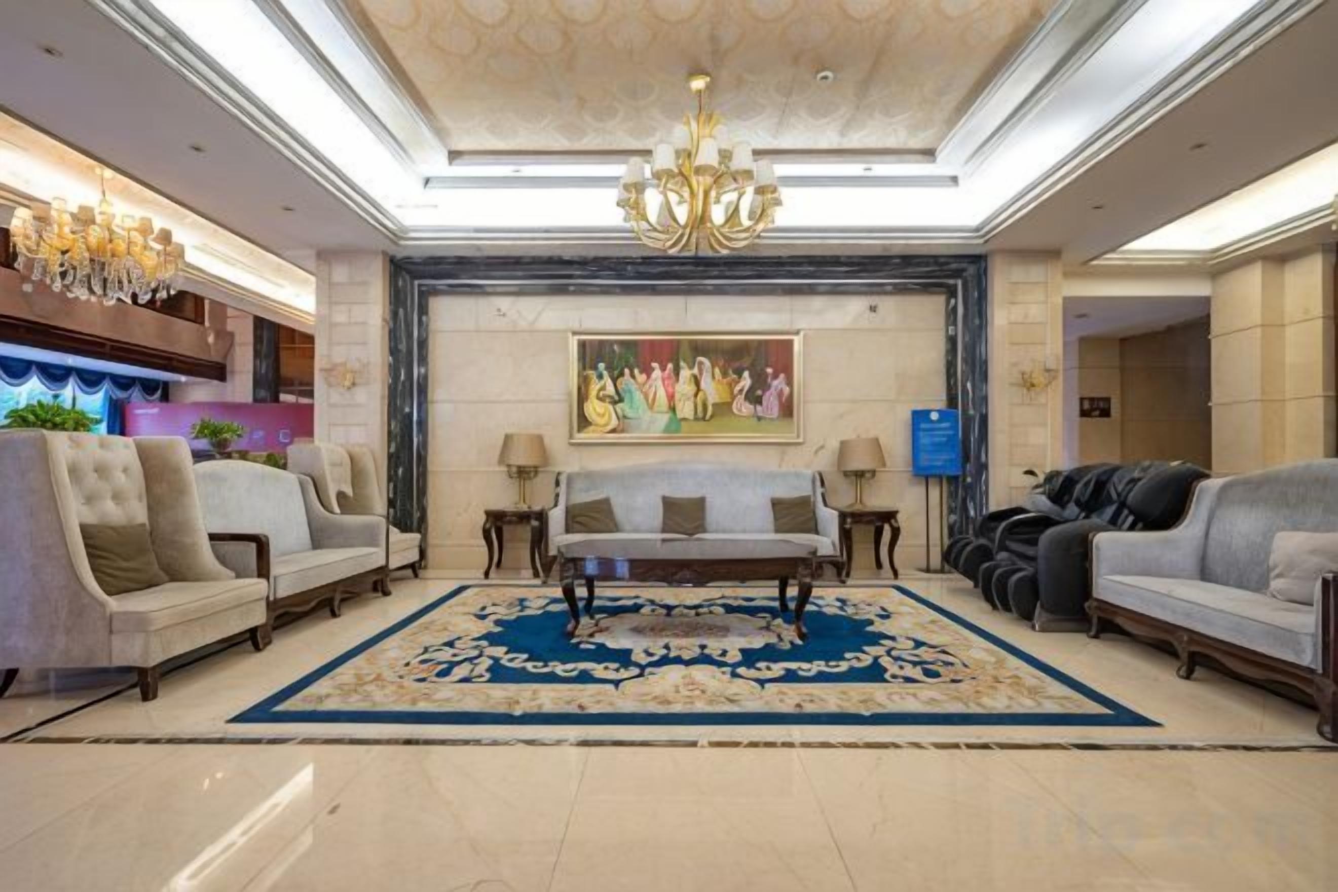 Una hall con divani, un lampadario, un tappeto grande e un quadro appeso al muro.