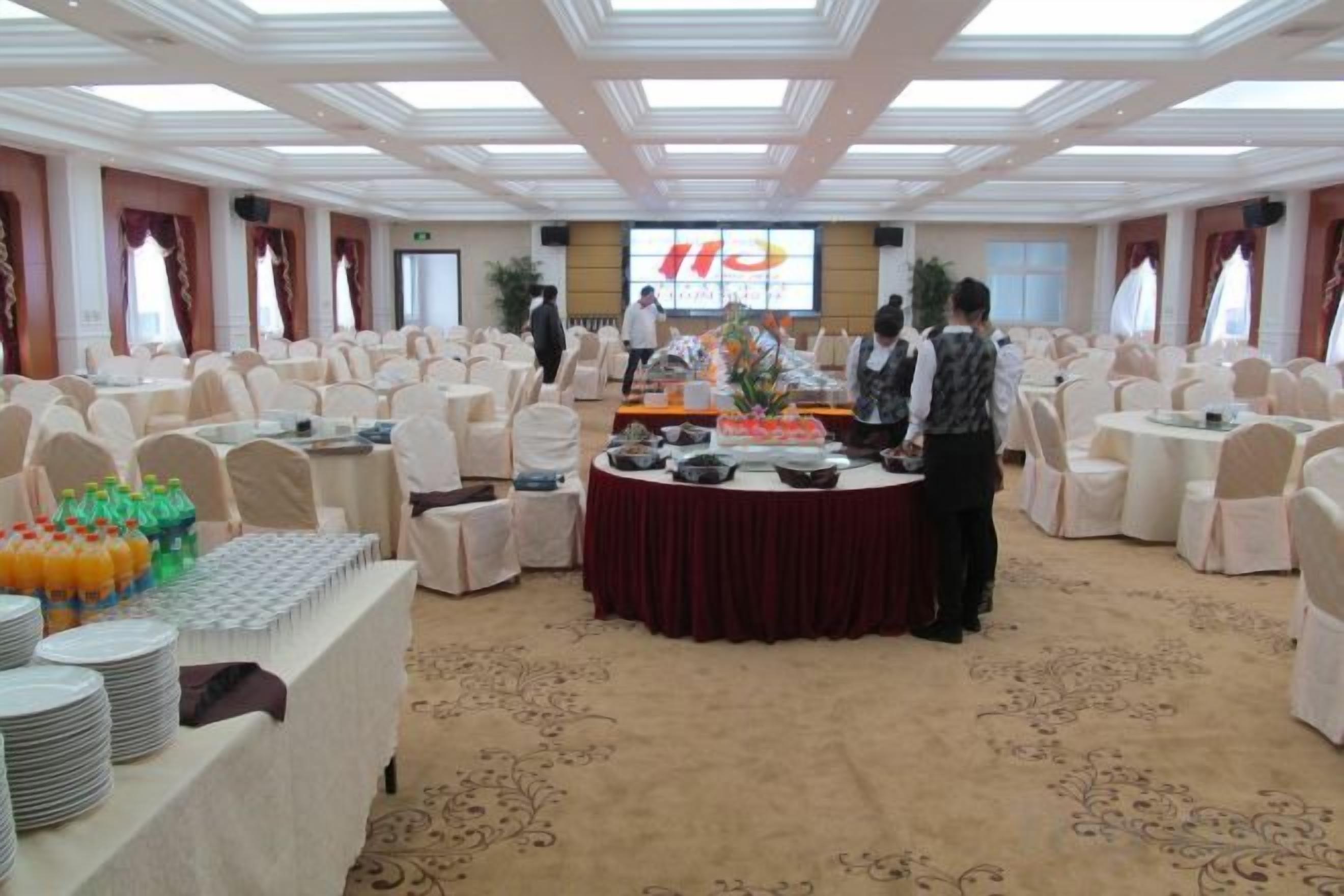 A banquet hall with round tables, chairs, and a buffet setup.